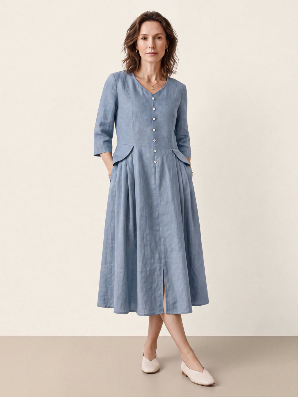 Woman wearing a light blue button-front midi dress with her hands in its pockets.