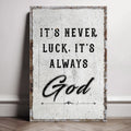 Distressed white canvas reading It's never luck. It's always God, leaning against a wall.