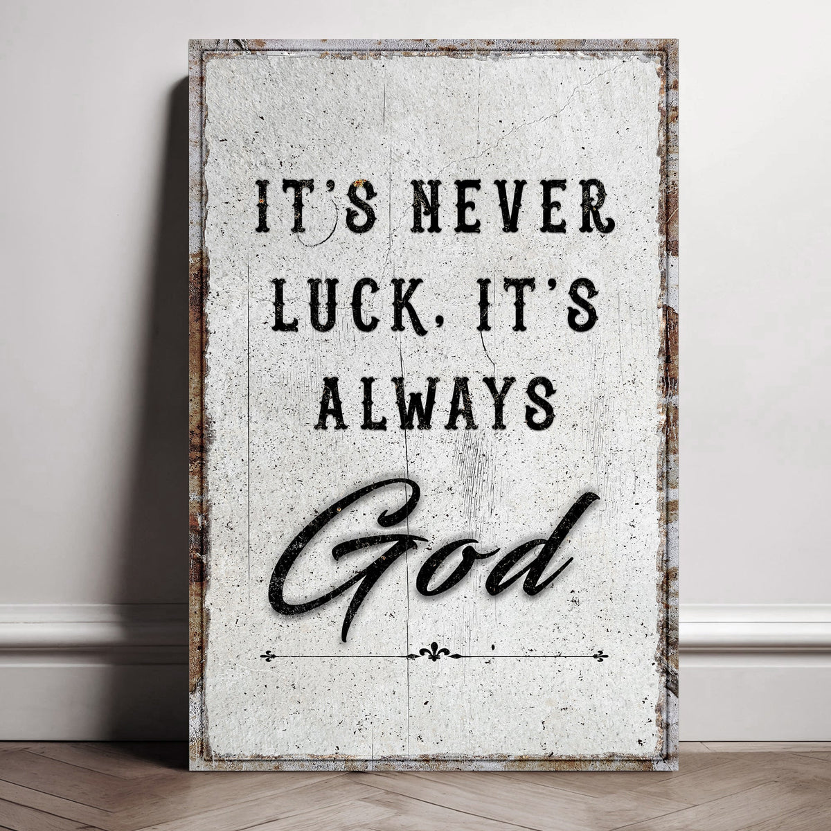 Distressed white canvas reading It's never luck. It's always God, leaning against a wall.