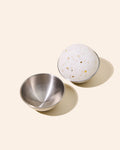 Open metal tin beside speckled round disc.