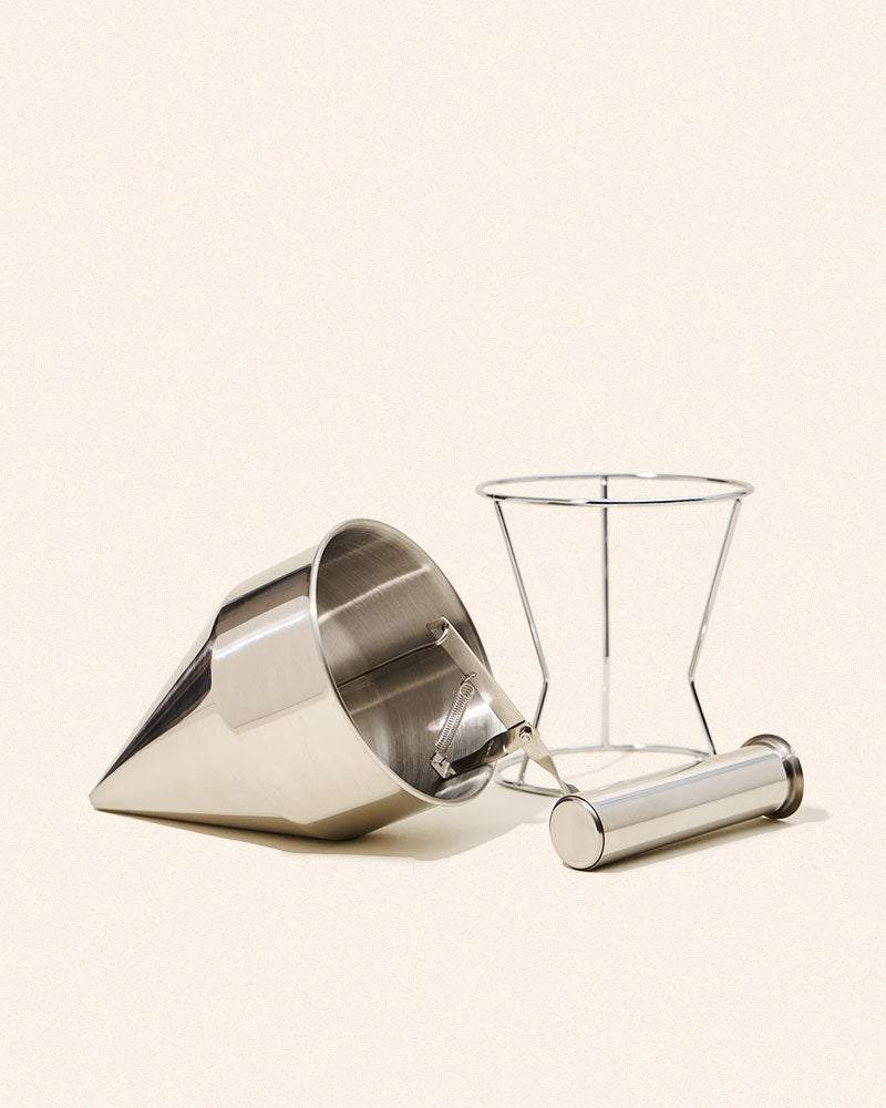Metal pouring pitcher beside wire stand.
