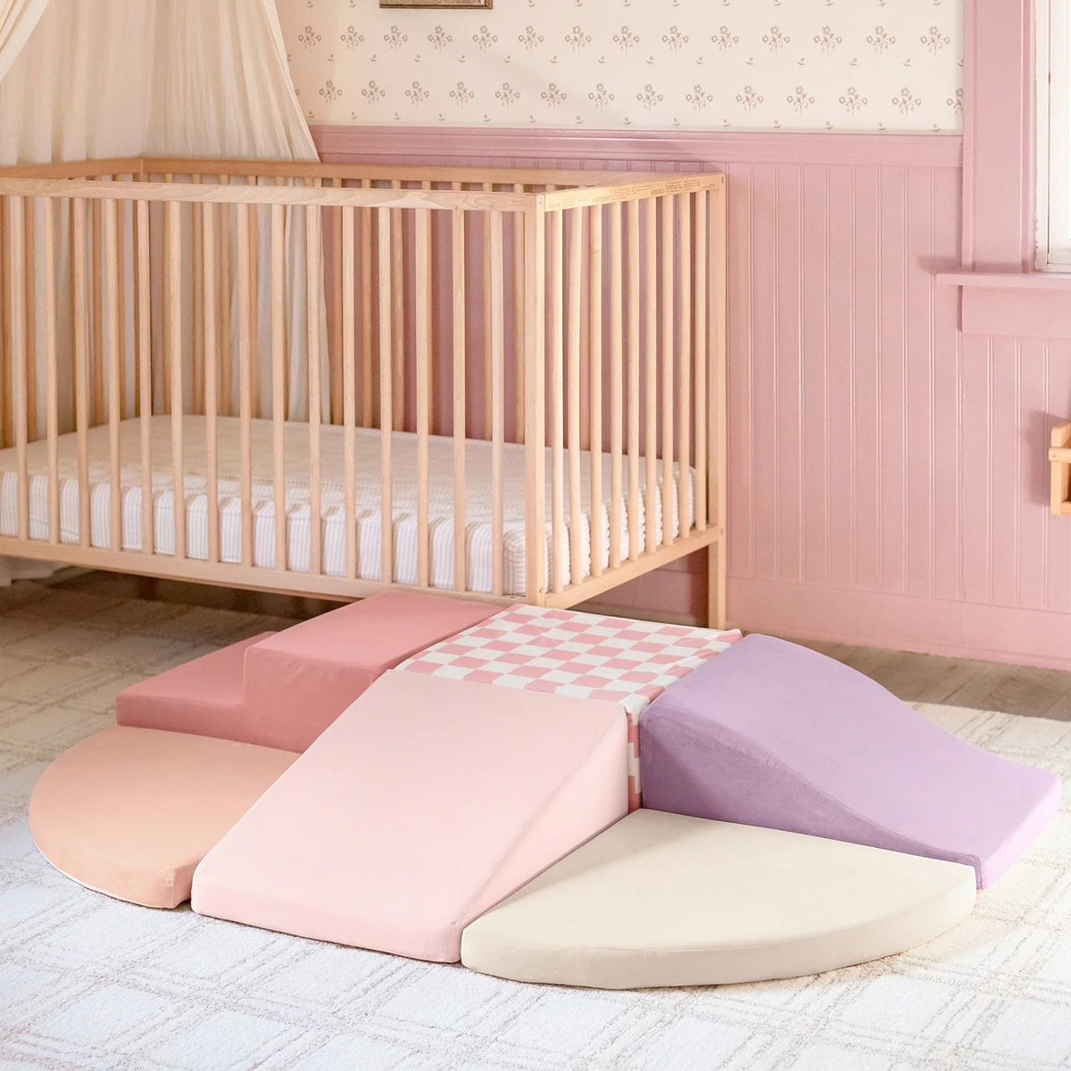 Pink foam climbing blocks beside a wooden crib.