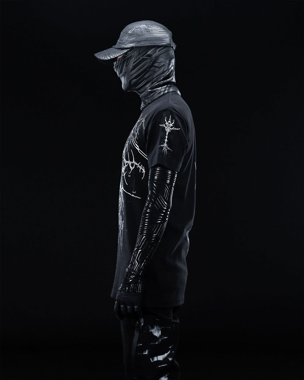 Side view of masked model wearing black T-shirt with fine gray ornamental artwork.