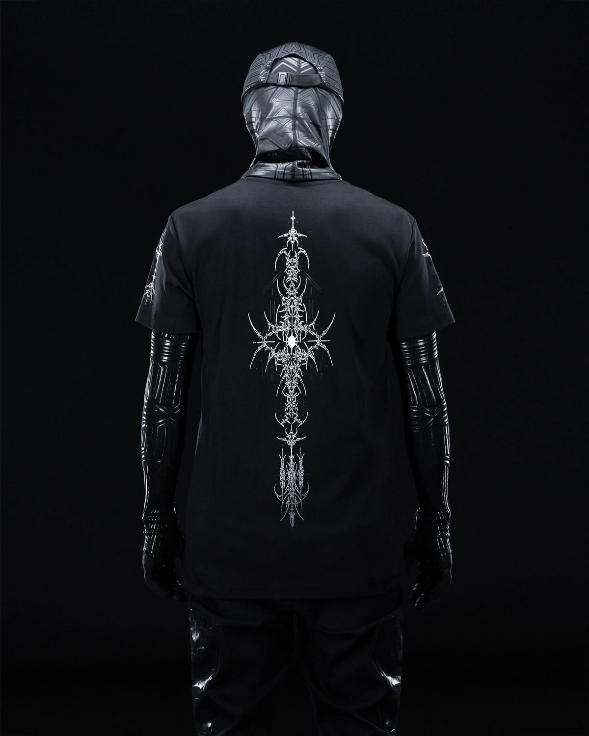 Rear view of masked model wearing black T-shirt with fine gray ornamental artwork.
