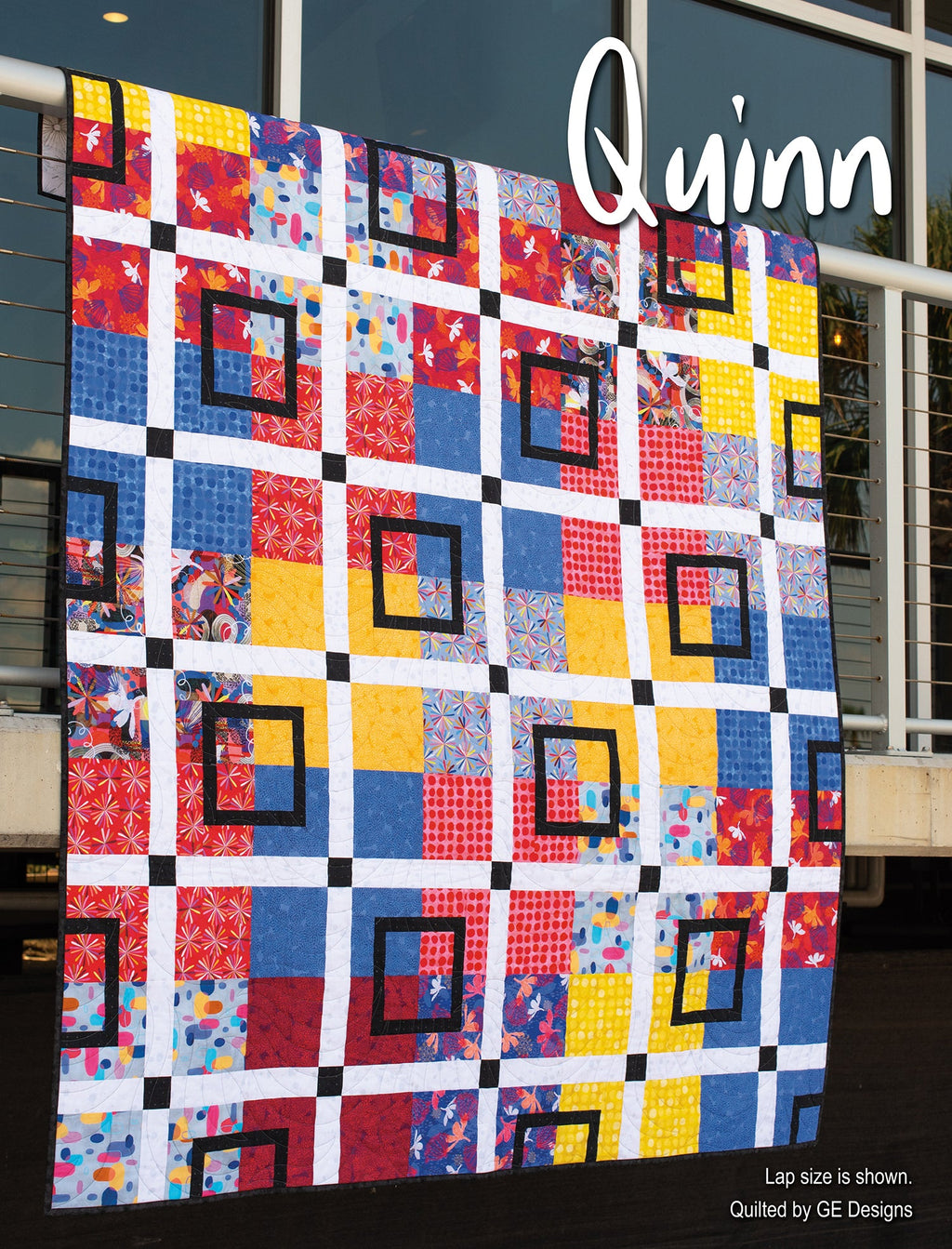 Multicolored grid quilt labeled Quinn hanging vertically.